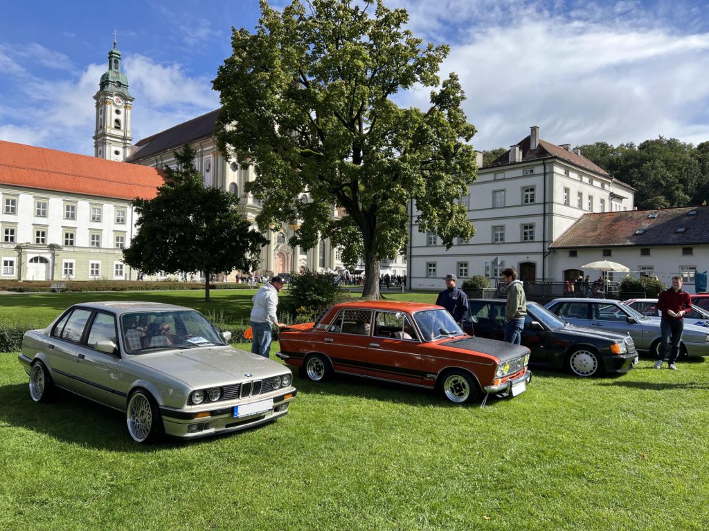 Oldtimer-Autotreffen als Event auf einer grünen Wiese vor historischer Klosterarchitektur bei Sonnenschein