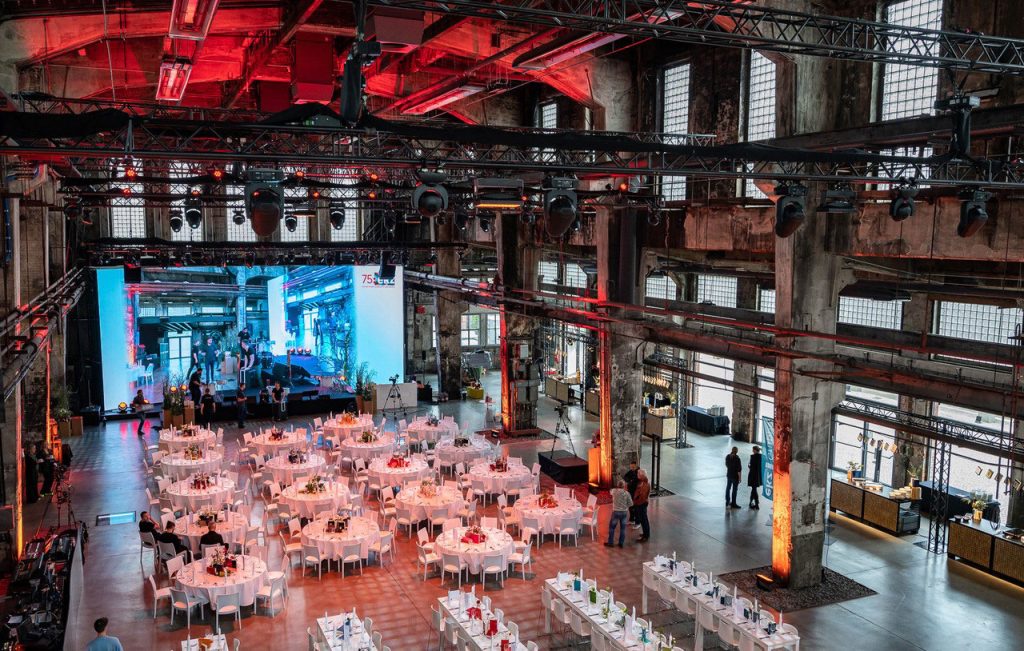 Moderne Eventlocation in einer Industriehalle mit gedeckten Tischen, Bühnenbild und roter Beleuchtung
