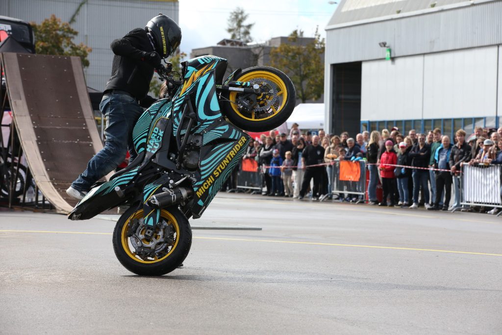 Motorradfahrer führt Stunt bei Event vor großer Menschenmenge in urbaner Eventlocation auf geöffnetem Platz vor