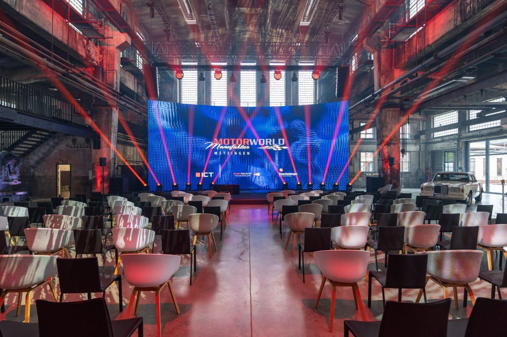 Moderne Eventlocation mit Bühne, LED-Leinwand und Bestuhlung in industriellem Ambiente für Veranstaltungen