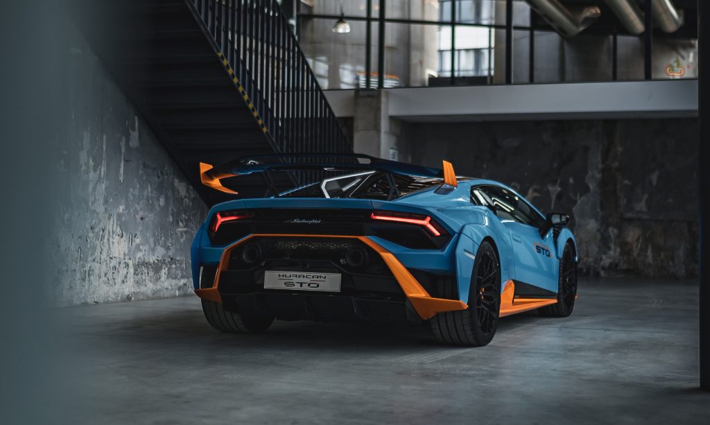 Blauer Lamborghini Huracan STO mit orangefarbenen Akzenten in einer Industriehalle als stilvolle Eventlocation