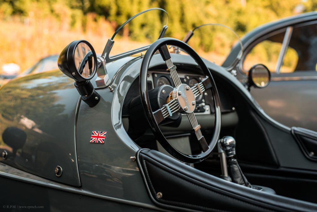 Detailaufnahme eines klassischen grauen Autos mit schwarzem Lenkrad und britischem Flaggenaufkleber