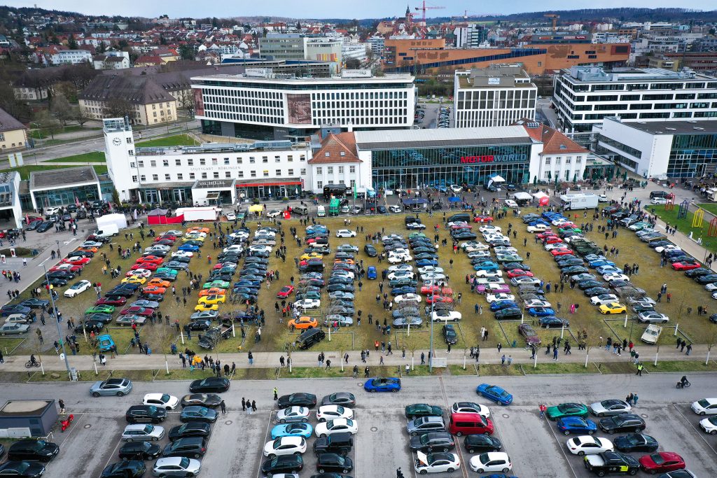 Großes Autoevent mit verschiedenfarbigen Fahrzeugen auf Rasenfläche vor moderner Eventlocation Motorworld Stuttgart-Böblingen