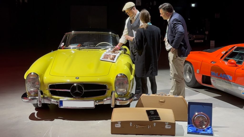 Drei Personen begutachten einen gelben klassischen Mercedes bei einem Event mit mehreren Oldtimern in der Eventlocation