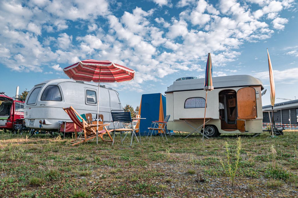 Outdoor-Event mit zwei Vintage-Wohnwagen, Sonnenschirmen und Campingstühlen auf einer Wiese unter blauem Himmel