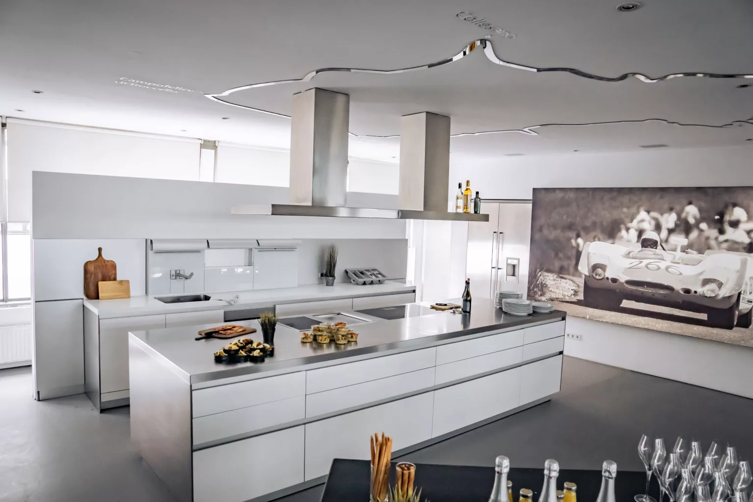 Modern event location with white kitchen island, stainless steel worktops and retro racing car picture on the wall