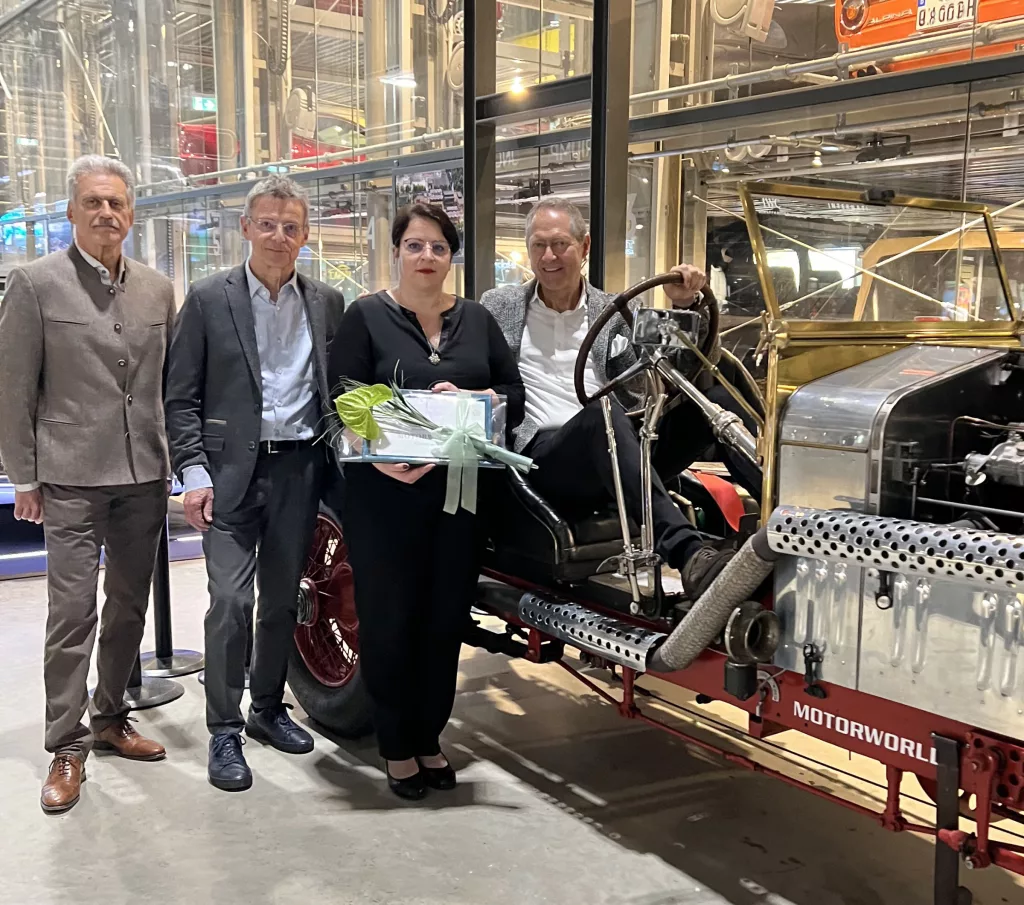 Vier Personen stehen bei einem Event neben einem Oldtimer-Auto in einer Eventlocation mit Industrie-Charme
