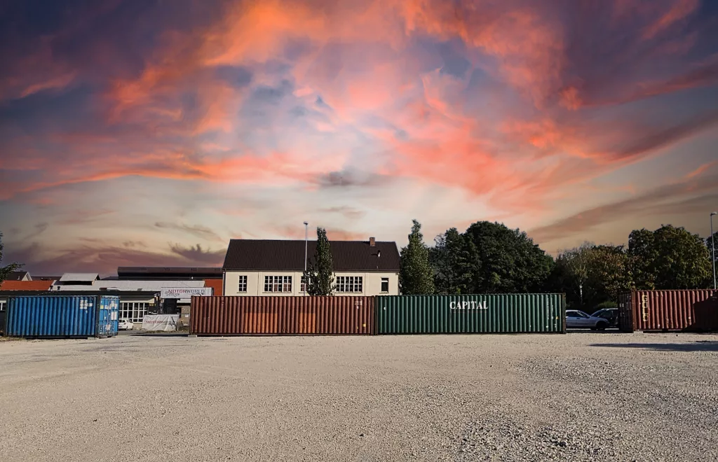 Offene Fläche mit bunten Containern vor Gebäuden unter einem dramatischen Sonnenuntergangshimmel, mögliche Eventlocation