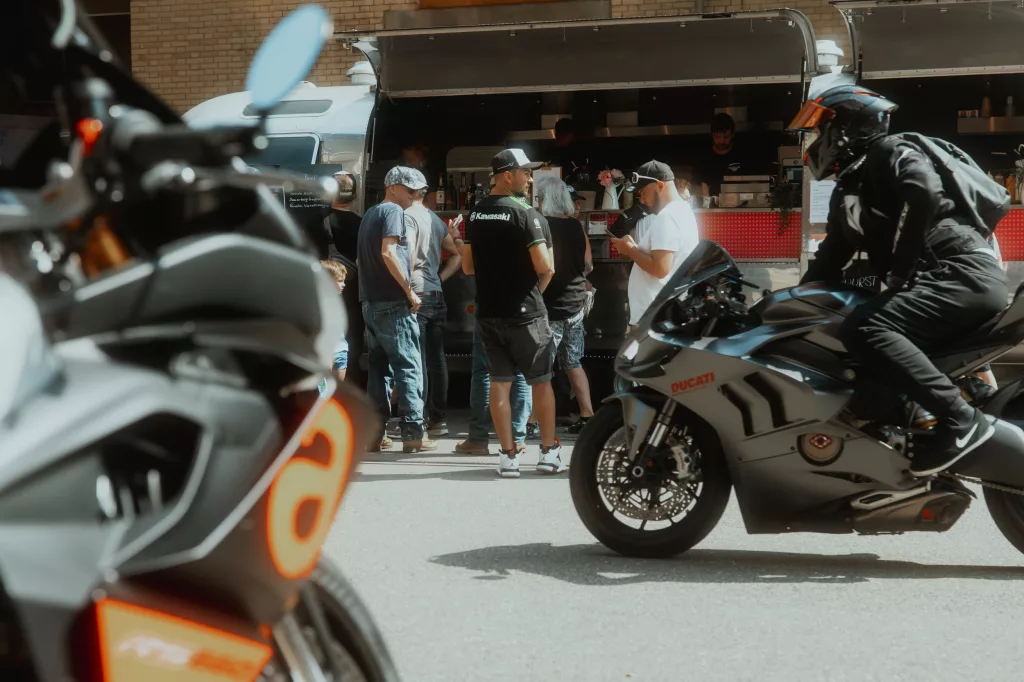 Motorradfahrer und Gäste bei einem Event vor einem Foodtruck als Eventlocation an einem sonnigen Tag