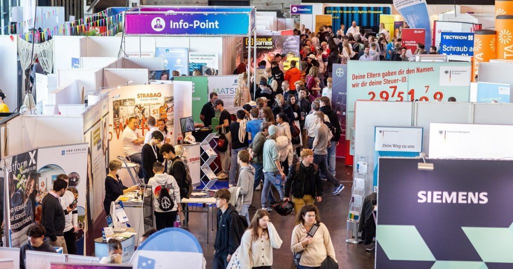Menschen auf einem vollen Event in einer großen Eventlocation mit verschiedenen Informationsständen und Bannern
