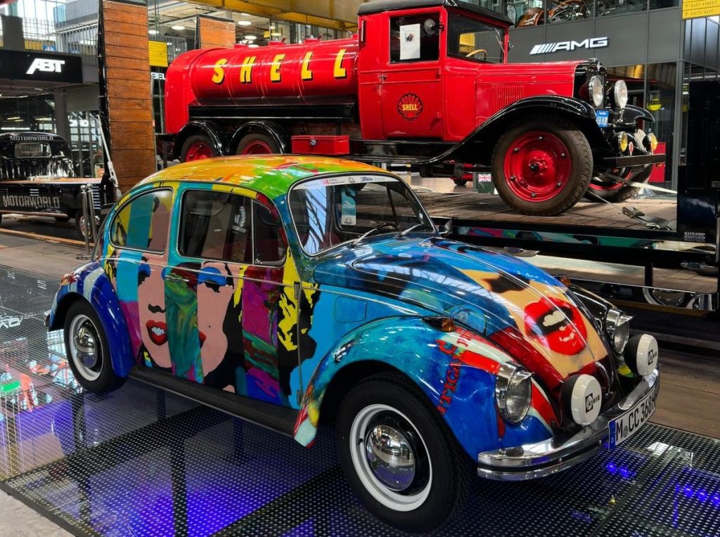 Bunter Oldtimer im Stil Pop Art vor rotem klassischen Shell-Tanklastwagen in moderner Eventlocation