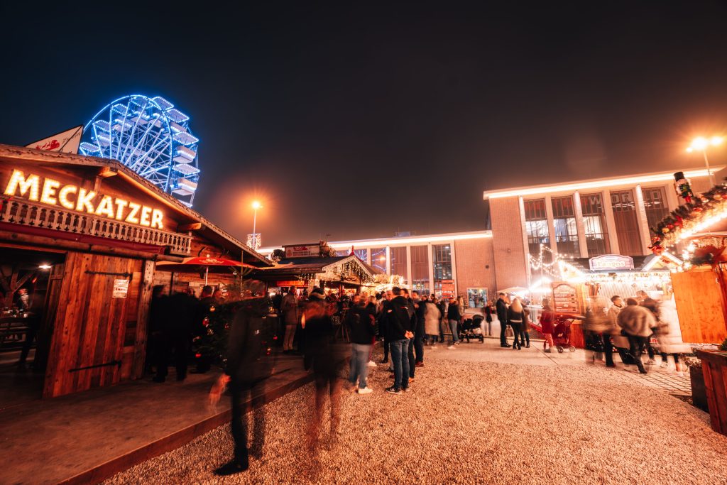 Abendliches Event auf Weihnachtsmarkt mit festlich beleuchteten Holzständen und großem Riesenrad im Hintergrund