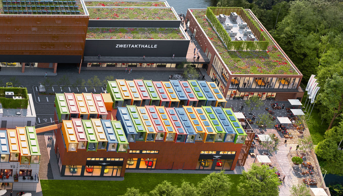 Aerial view of a modern building complex with planted roofs, colorful modular houses on the roof of a house, large terrace with seating areas and adjacent water as well as green wooded surroundings.