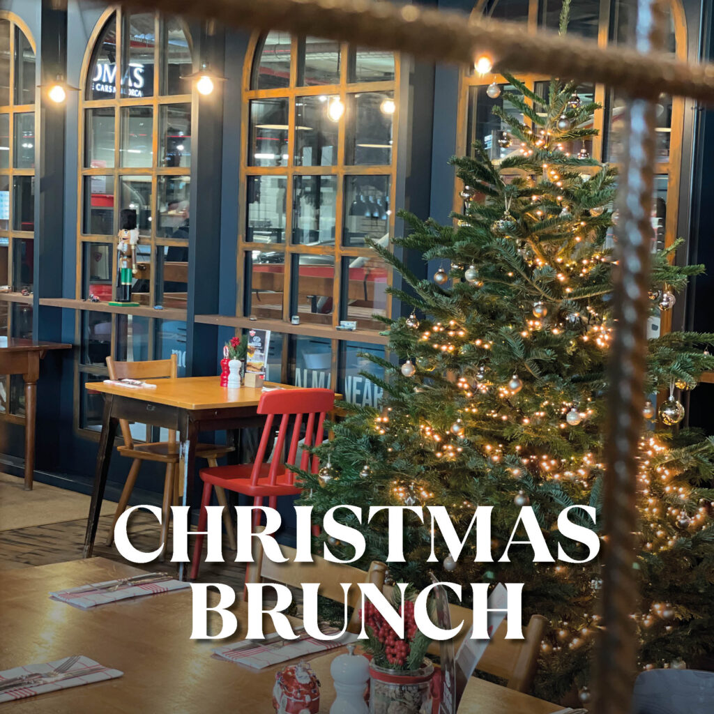 Weihnachtlich dekorierter Tannenbaum mit glänzenden Kugeln und warmen Lichterketten in einem gemütlichen Restaurant, daneben ein Holztisch mit rotem Stuhl und Fensterfront; weiße Schrift CHRISTMAS BRUNCH überlagert das Bild.