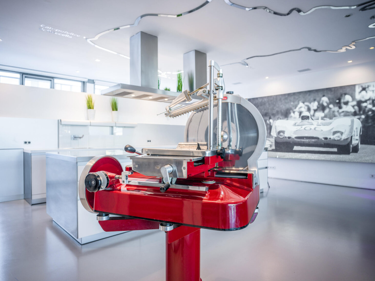 Rote Aufschnittmaschine auf Säule in moderner Küche, im Hintergrund großformatiges Schwarzweißfoto eines Rennwagens.