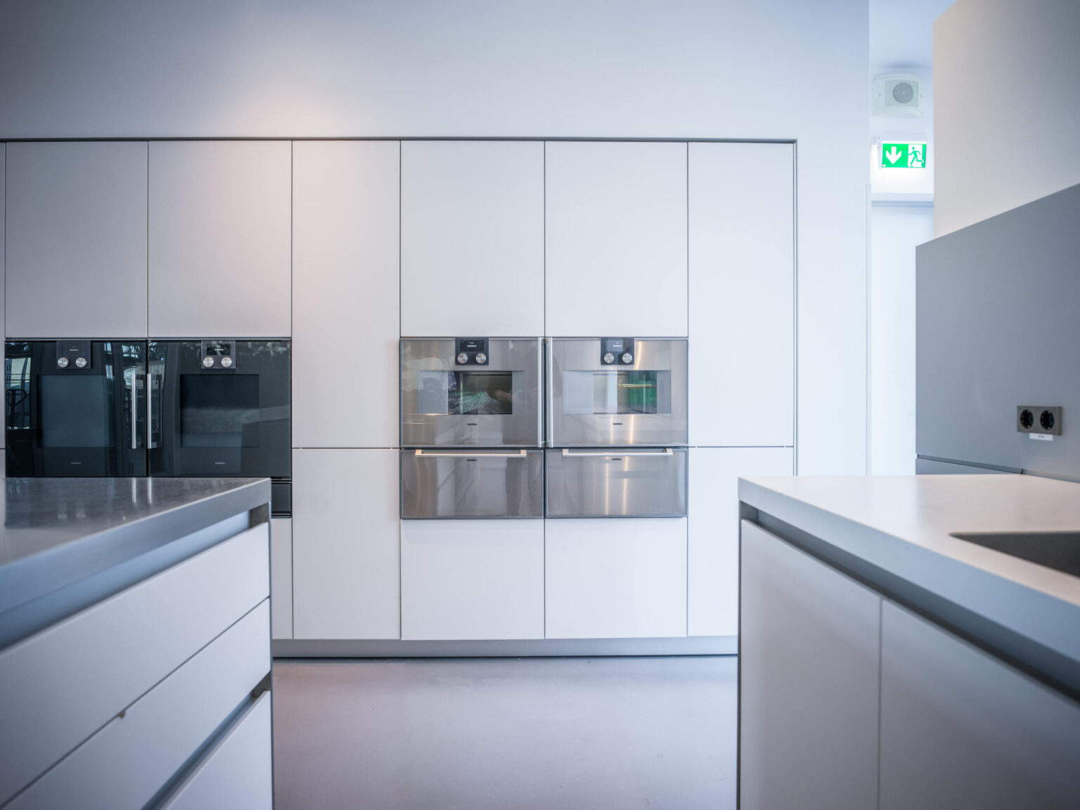 Moderne, minimalistische weiße Küche mit eingebauten Edelstahl-Backöfen und klaren Arbeitsplatten.