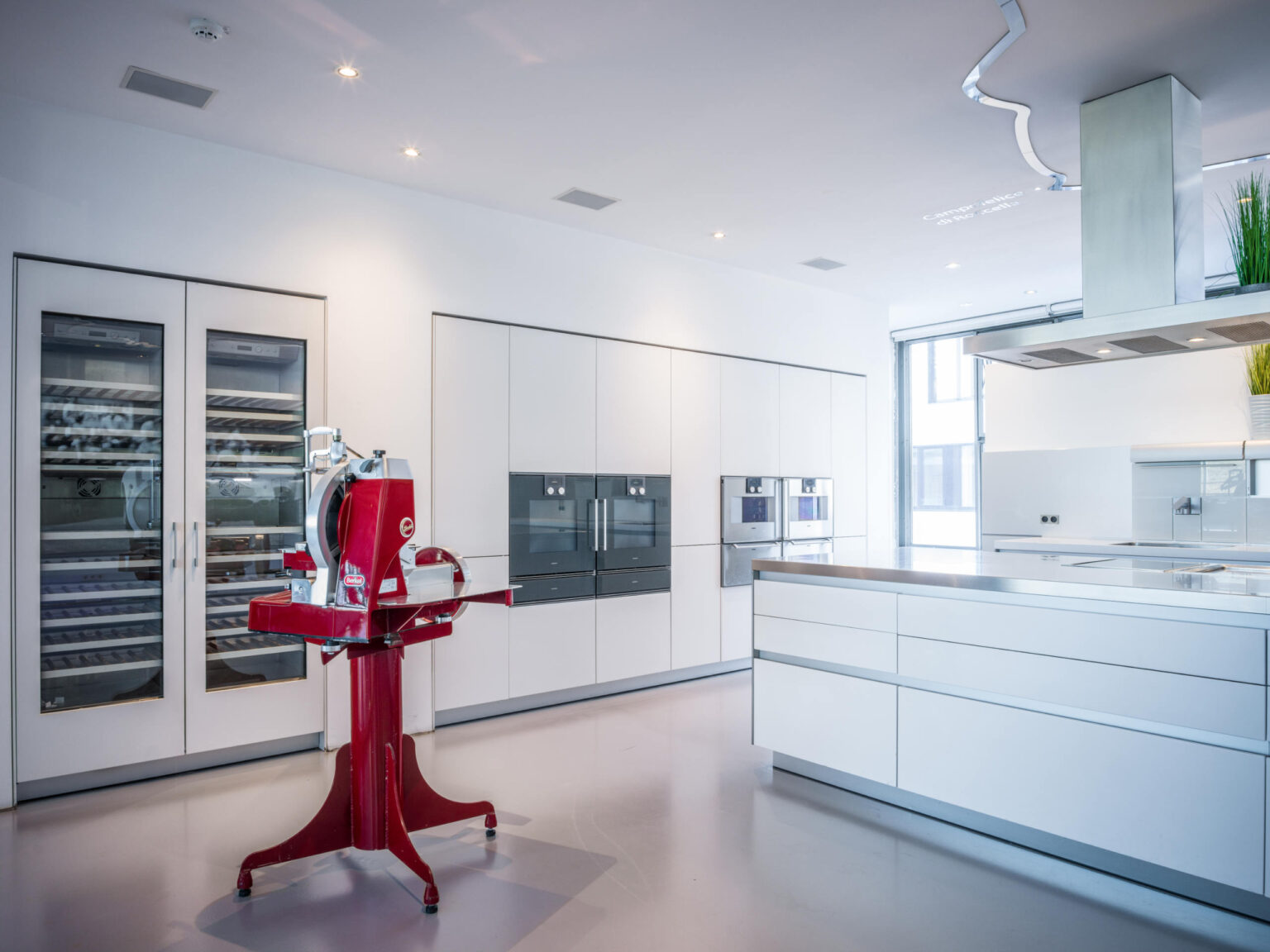 Moderner heller Küchenraum mit großer Insel und auffälligem roten Stand-Aufschnittschneider in der Mitte.