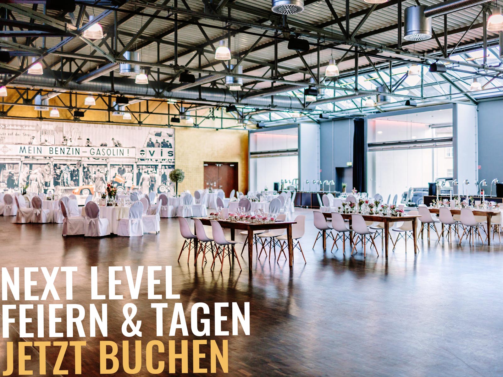Große Industrie-Eventhalle mit gedeckten Tischen, weißen Stühlen, sichtbarer Metallträgerdecke und Werbetext "Next Level – Jetzt buchen".