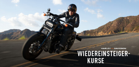 Motorradfahrer mit Helm und Lederjacke lehnt in einer Kurve auf einer Landstraße; rechts unten Schriftzug Wiedereinsteiger-Kurse.