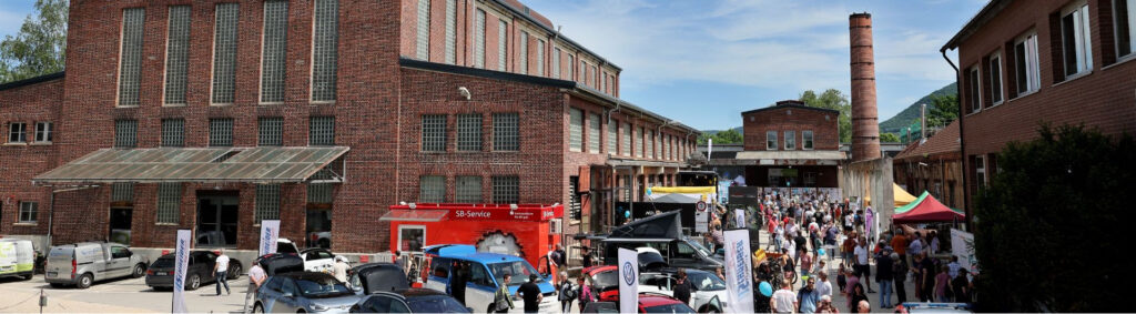 Belebte Messe im Innenhof alter roter Backsteingebäude mit Verkaufsständen, vielen Besuchern und ausgestellten Autos.