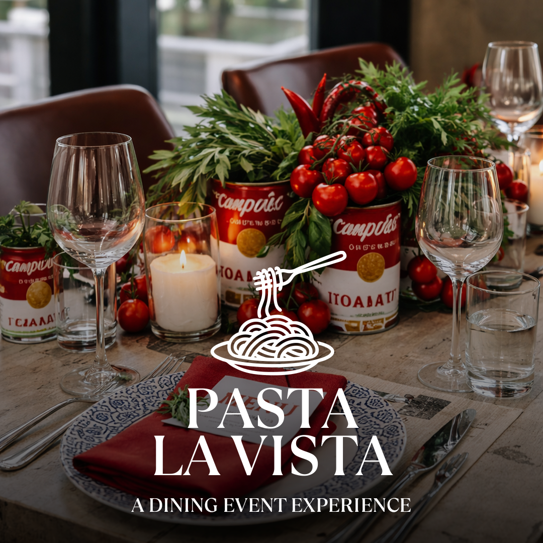 Tisch gedeckt mit Pasta-Deko: Tomatendosen und Rispen, Weingläser, Kerze und Schriftzug Pasta La Vista.