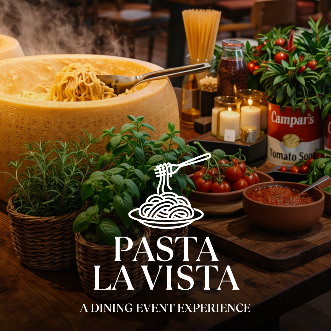 Tisch mit Pasta im Parmesanrad, frischen Kräutern, Tomaten und dem Schriftzug Pasta La Vista.