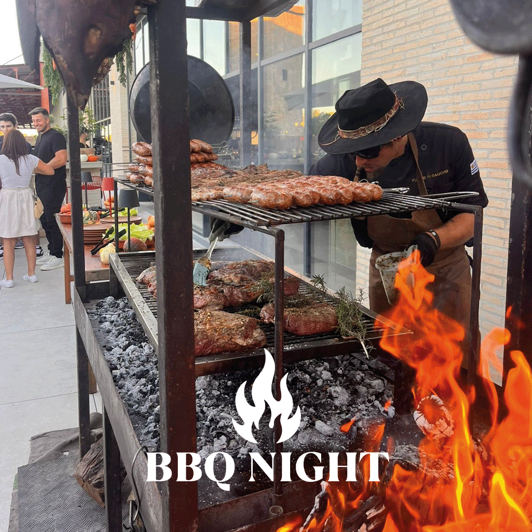 Grill master in a hat turns sausages and steaks on an open charcoal grill at an outdoor BBQ night.