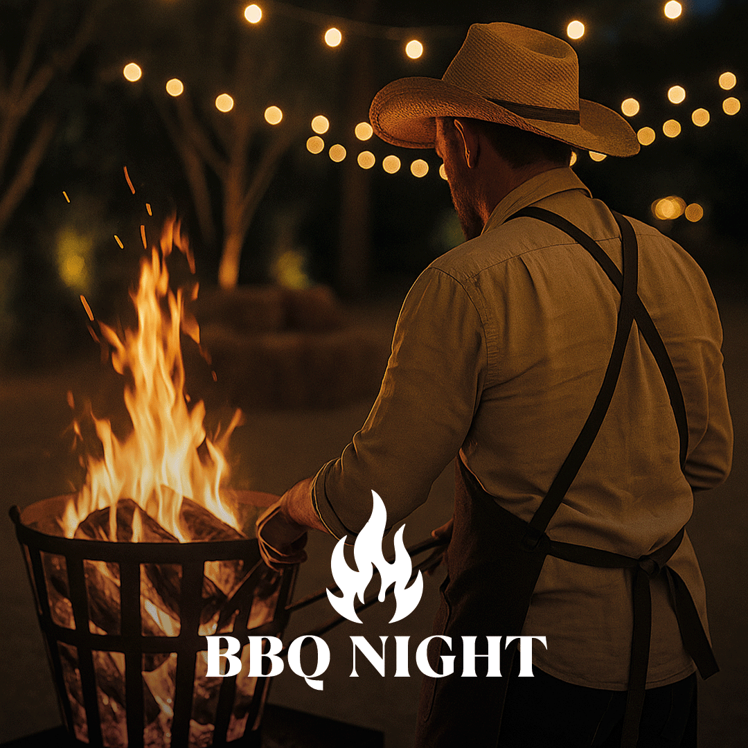 Mann mit Cowboyhut und Schürze zündet abends an einem Feuerschalen-Grill Feuer bei Lichterketten im Hintergrund.