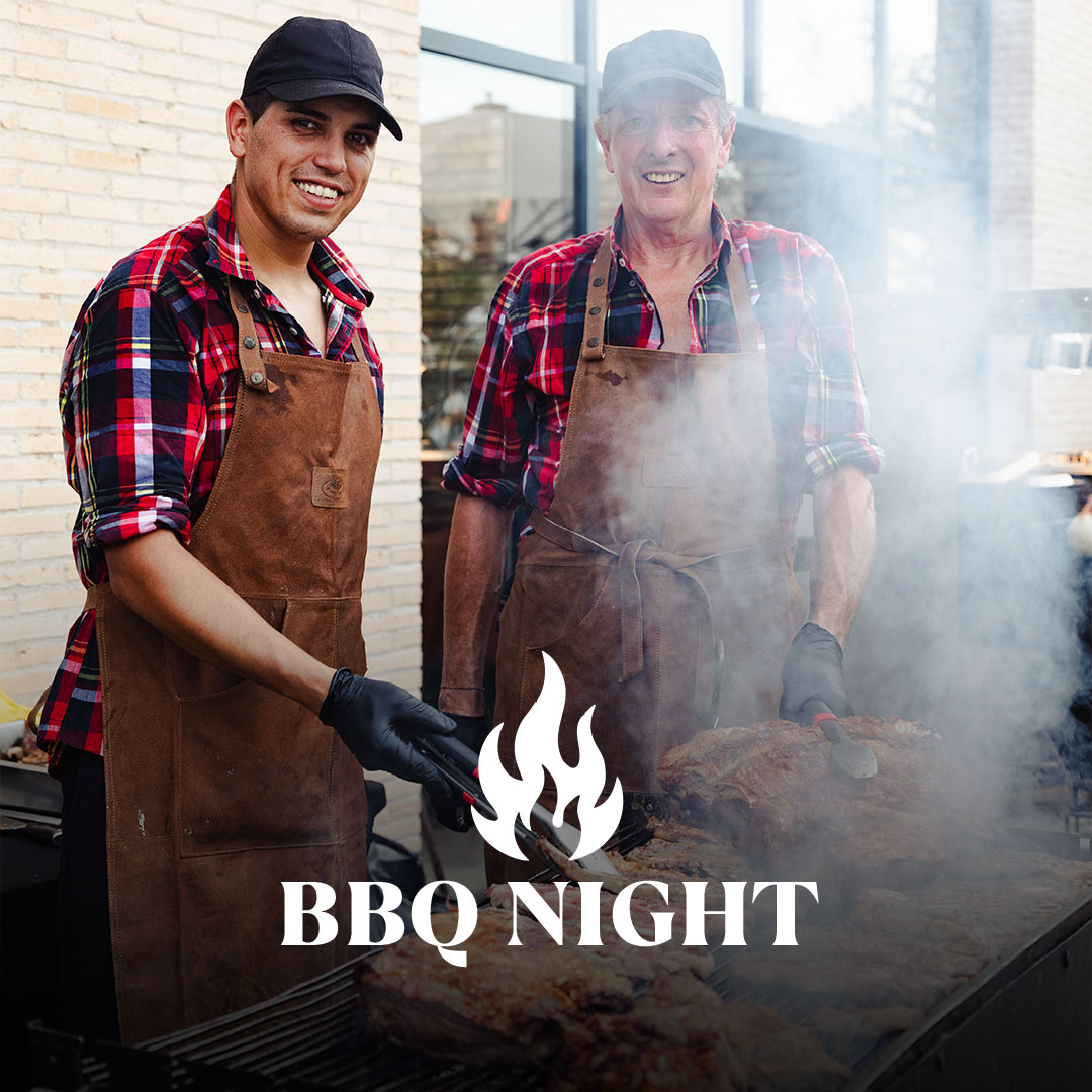 Zwei Männer grillen bei einer BBQ-Night Steaks und stehen am rauchigen Grill