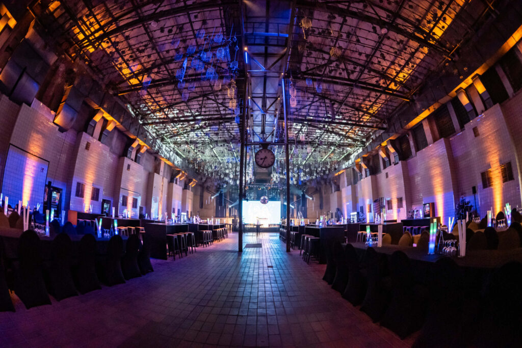 Große Eventhalle mit buntem Licht, Tischen und Bühne am Ende