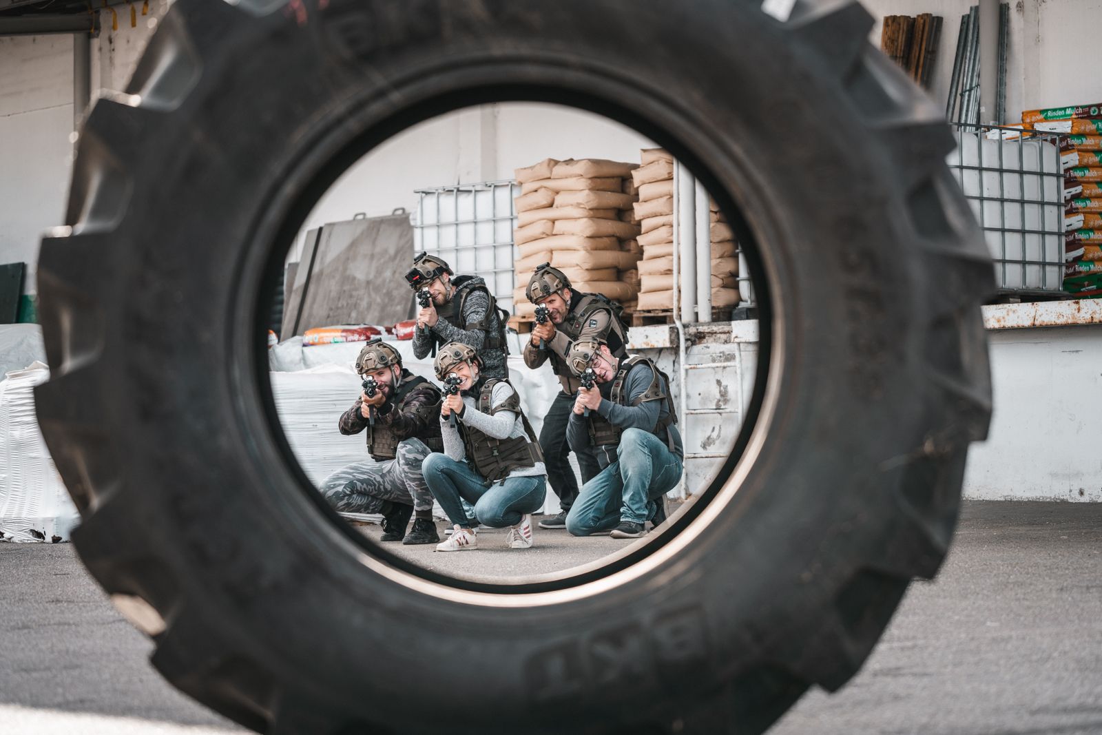 Gruppe von Personen in Taktikausrüstung zielt mit Markierern durch einen Reifenrahmen