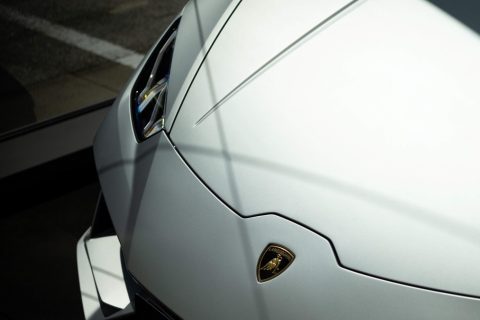 Vorderer Teil eines weißen Lamborghini-Sportwagens mit sichtbarem Lamborghini-Emblem auf der Motorhaube, teilweise im Schatten.