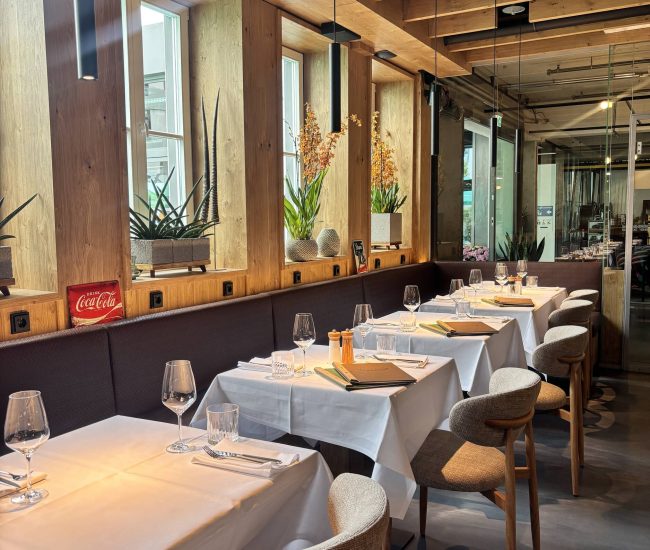 Modernes Restaurant mit gedeckten Tischen, Holzdecke und stimmungsvoller Beleuchtung