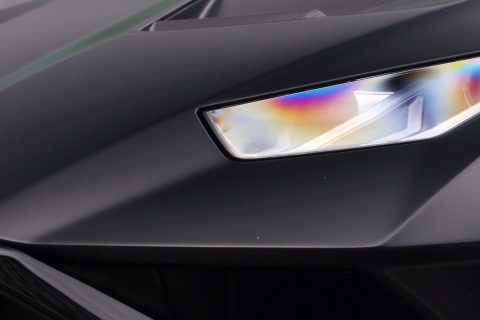 Nahaufnahme eines mattschwarzen Sportwagens, Fokus auf der linken Scheinwerferpartie und der Motorhaube mit ziegelrotem GTD-Logo, im Hintergrund ein grünes Auto seitlich zu sehen.