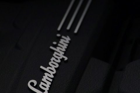 Nahaufnahme eines schwarzen Motorteils mit dem weißen Lamborghini-Logo und drei parallelen Linien darauf