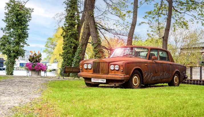 Rusty vintage car in event location at green park with trees and view of water in the background