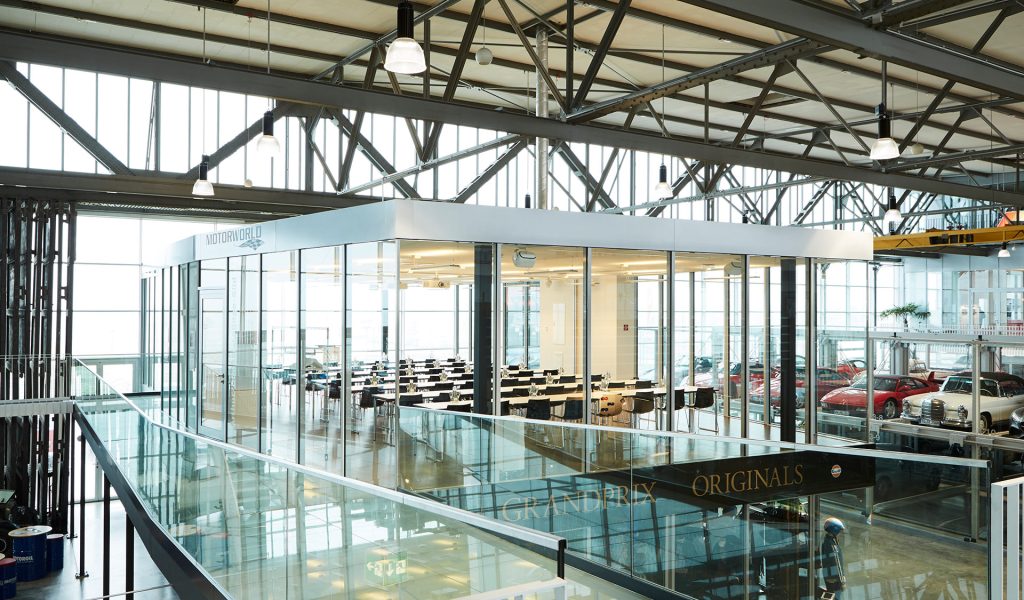 Modern event location with glass walls and rows of tables in an industrial hall with vintage cars