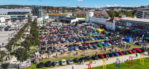 Großes Autoshow-Treffen auf einer Freifläche vor Messegebäuden mit zahlreichen Besuchern und farbenfrohen Fahrzeugreihen.