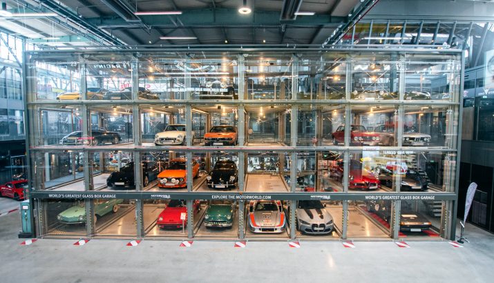 Multi-storey glass parking garage with illuminated compartments in which classic and sports cars are on display.