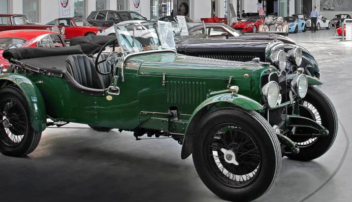 Green vintage convertible in a large event location with other classic vehicles in the background